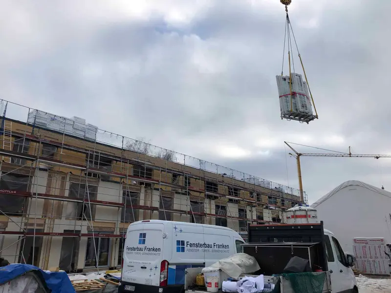 Ein Kran hebt neue Fenster auf einen Rohbau, davor der Transporter von Fensterbau Franken
